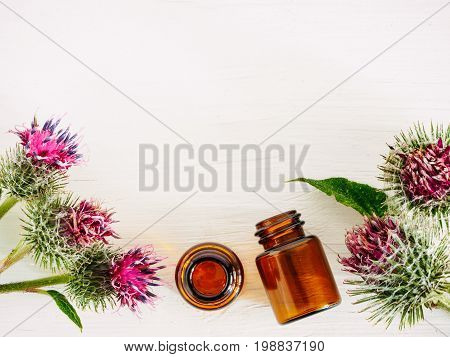 burdock oil in small glass bottle and burdock flowers on white wooden table. Top view or flat lay. Copy space.
