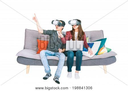 Young Asian couple playing VR virtual reality gadget sitting on sofa together isolated on white background. Modern entertainment technology VDO game devices or family hobby activity concept