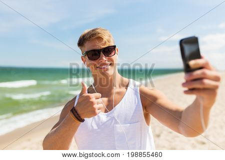 summer holidays and people concept - happy smiling young man with smartphone taking selfie on beach