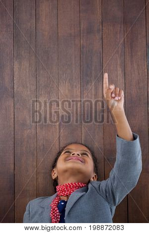 Smiling businesswoman pointing up wards while standing with head back against wooden wall