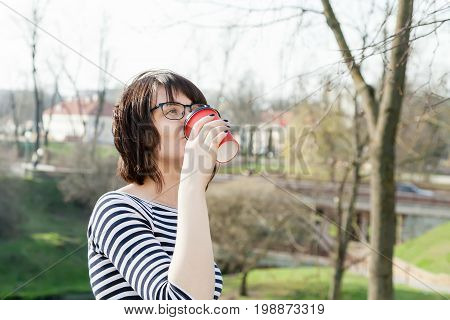 A girl in a striped T-shirt is drinking coffee with a blurred background