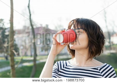 A girl in a striped T-shirt is drinking coffee with a blurred background