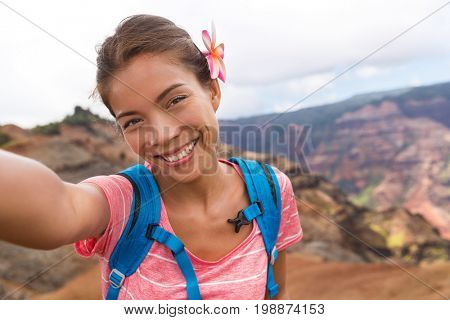 Selfie travel tourist hiker girl in Waimea Canyon Hawaii hike taking self-portrait picture with camera phone having fun hiking in Kauai mountains, Hawaii. Woman taking photos on adventure travel.