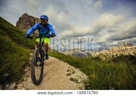View of cyclist riding mountain bike on single trail in Dolomites, Cinque Torri, South Tirol, Italy