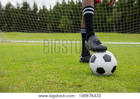 Low section of male soccer player with ball on field by goal post