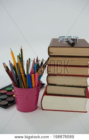 Close-up of book stack, magnifying glass, color pencils and palette on white background