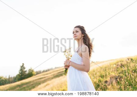 Curly young woman with a bunch of chamomiles enjoying the view in the top of mountain on a hot summer day. young pretty woman closeup. Lifestyle concept