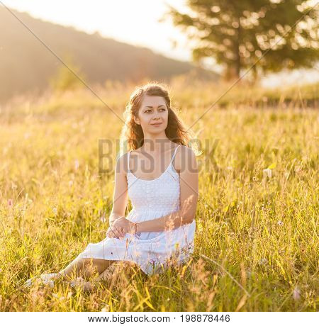 Young pretty curly woman sitting and enjoying on the mountains top. Beautiful young cheerful female model.Young woman outdoors. Mountains landscape on background. Freedom concept.