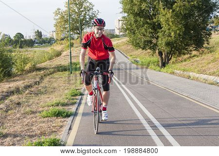 Sport and Cycling Ideas. Portrait of Professional Male Cyclist Doing Uphill Out of the Saddle on Road Bike. Fully Equipped in Professional Outfit. Horizontal Image Composition