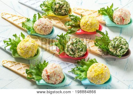 Small snack balls on serving spoons. Tasty balls of cream cheese with aromatic herbs surimi garlic and egg. Delicious appetizer for party or banquet. Festive food