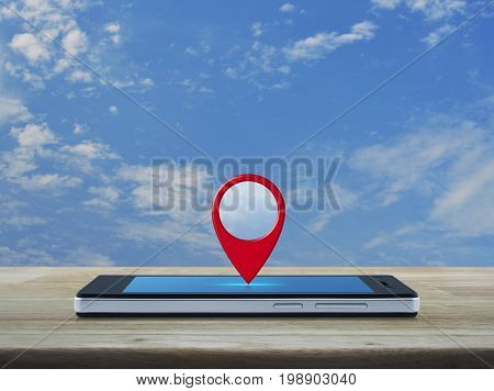 Map pin location button on modern smart phone screen on wooden table over blue sky with white clouds Map pointer navigation concept