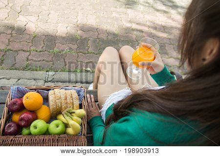 Young Woman Holding Glass Drinking Orange Juice With Friuits Basket. Top View From Back. Healthy Con