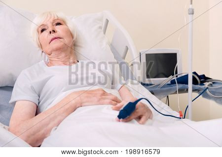 Many devices. Vulnerable sore senior lady resting on bed and restoring her strength while recovering from heart stroke