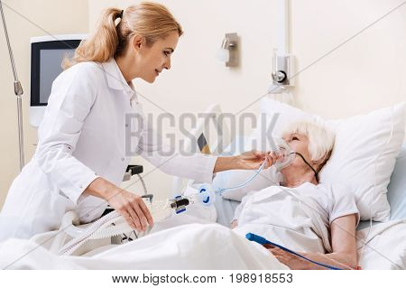 We will use some devices. Wise young energetic woman treating her patient and making her wearing oxygen mask for ensuring her proper breathing