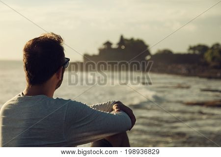 Modern man sitting on the beach and enjoying the view.