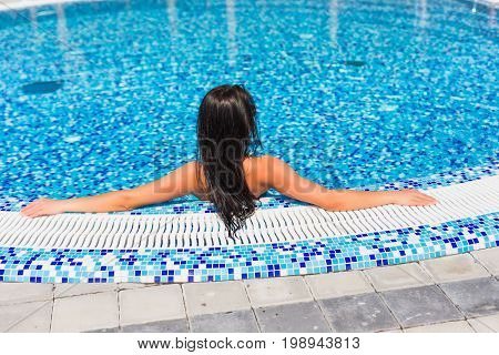 Beautiful Girl In A Bathing Suit Sits On The Edge Of The Pool, The View From The Back
