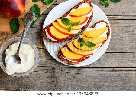 Simple rye sandwiches with soft cheese and fresh nectarines slices. Bright summer sandwiches on a plate. Vintage wooden background with copy space. Top view