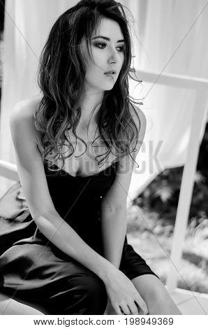 Young Girl In A Long Evening Dress Is Sitting On A Chair. Black And White Photography