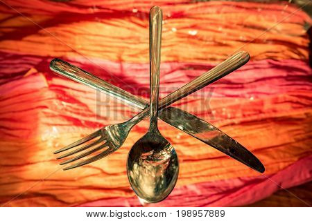 Fork, spoon and knife crossed against colorful background