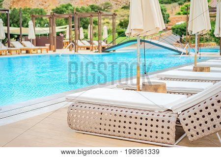 Sunbeds and sun umbrellas on the background of the recreation area near the swimming pool close-up. The background is blurred