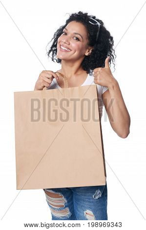 Happy mixed race woman holding craft shopping bag with blank copy space and gesturing thumb up