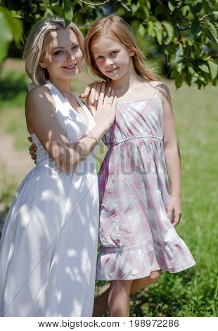 Beautiful mom and daughter posing for picture in garden. Family concept, mother and her daughter spending time in the gerden.