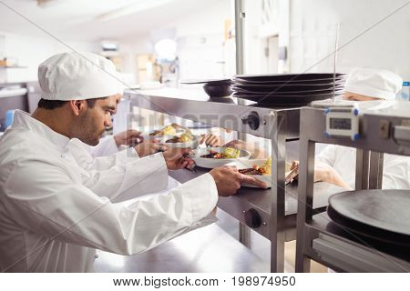 Chefs passing ready food to waiter  at order station in commercial kitchen