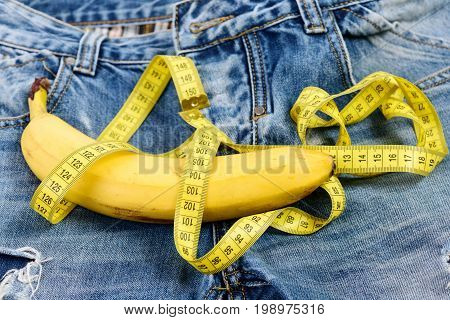 Jeans belt loops zipper and pocket close up. Health and male sexuality concept. Mens denim pants crotch with banana imitating male genitals. Banana wrapped with yellow measure tape on jeans.