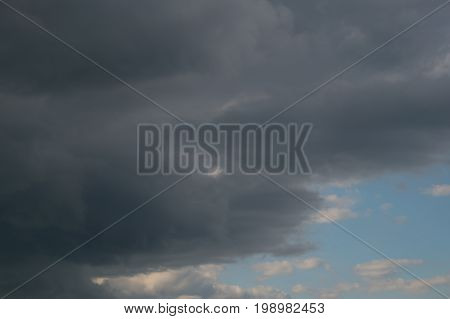 Grey dark fkuffy clouds on the blue sky at sunset or sunrise. Stormy weather.