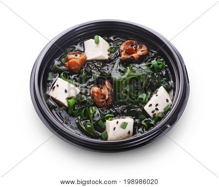 Japanese food delivery. Miso soup with tofu cheese, mushrooms and seaweed in black take away plate isolated at white background