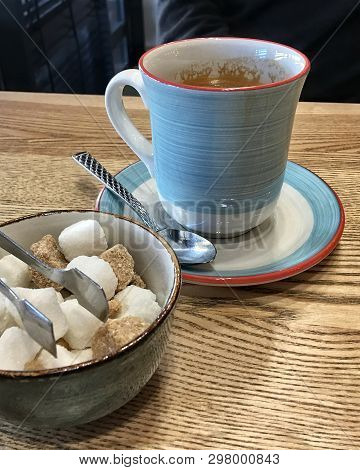 Coffee And Sugar On A Cafe Table Close To A Window. Nice Blue Coffee Cup, Saucer And A Teaspoon. Fan