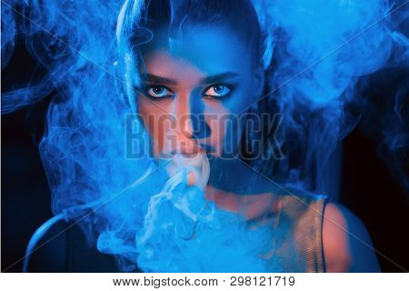 Young Woman Smoking Vape Or E-cigarette In Neon Blue Light