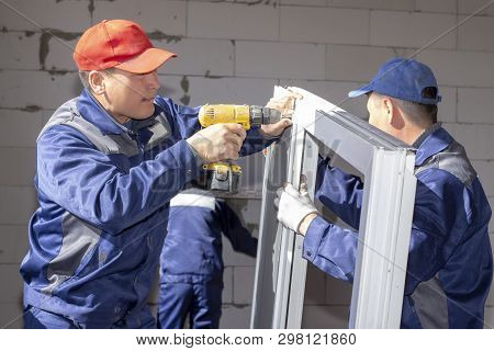 Workers Install Glazing In A House Under Construction, Make Measurements, Drill, Saw Grinder