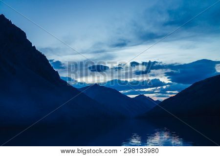 Amazing Blue Silhouettes Of Mountains On Dusk. Dawn Sky Reflected In Mountain Lake. Wonderful Atmosp