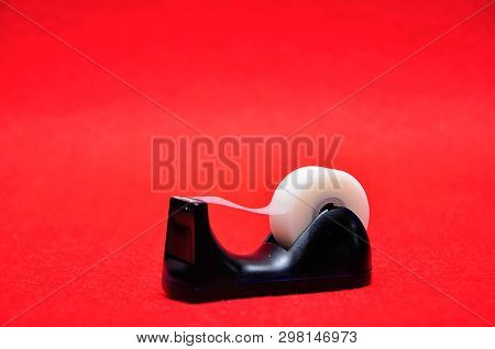 A Black Sellotape Holder With A Roll Of Sellotape On A Red Background