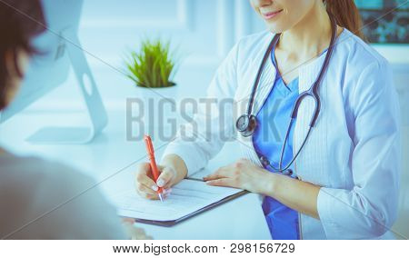 Doctor and patient discussing medical problems in a hospital consulting room. Doc filling in a patient's form