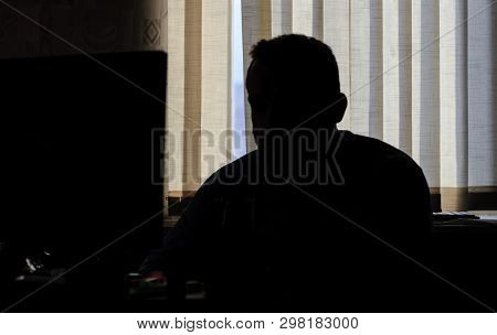 Man Sits In The Office At The Computer. Only Silhouette. He Looks At The Cameras On The Monitor