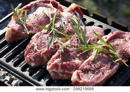 Cooking Outdoors. Raw Juicy Beef Steaks With Rosmary On Grill.