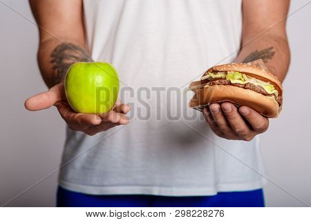 Concept Man Makes The Choice Between Healthy And Unhealthy Food. The Choice Between A Burger And An 