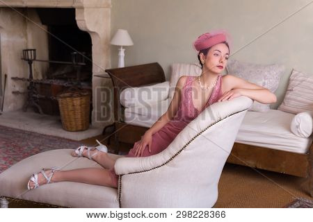 Sensual 1920s woman in pink flapper dress sitting on an antique chaisee longue or recliner
