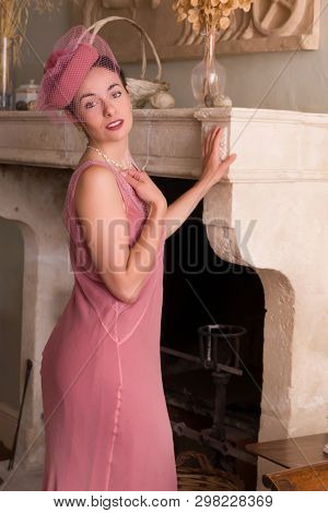 Vintage interior with 1920s flapper dress lady standing at an antique fireplace