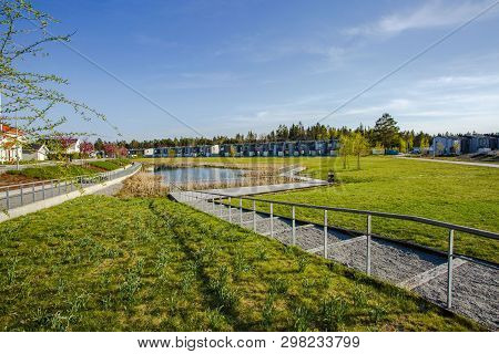 Amazing View Of Suburbian Landscape. Path To Little Pond And Cute Compact Suburbian Houses On Blue S