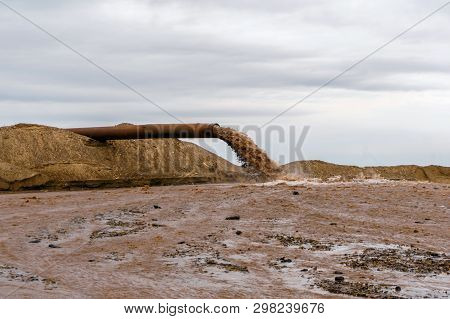 Rusty Pipe On The River Bank, From Which Sewage Flows, Dirty Sand Slurry
