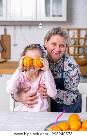 Happy Little Girl And Her Grandmother Have Breakfast Together In A White Kitchen. They Are Having Fu