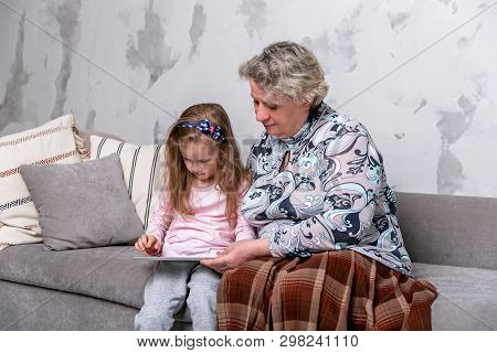 Grandmother And Her Little Granddaughter Are Watching Movies Together And Playing On The Device Whil