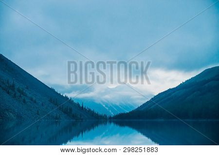 Amazing Silhouettes Of Mountains And Low Clouds Reflected On Mountain Lake. Beautiful Ripples On Wat