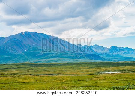 Huge Mountain Range At Overcast Weather. Creek And Little Lake Before Giant Mountains Under Cloudy S