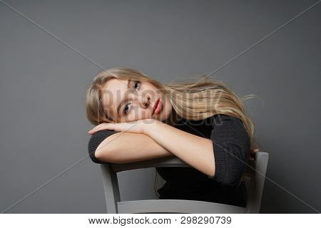 Bored Young Woman Sitting Astride On Chair - Gray Background With Copy Space