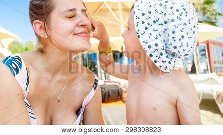 Portrait Of Smiling Happy Toddler Boy Applying Sunscreen Lotion On Mothers Face On Th Esea Beach