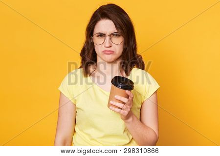 Miserable Upset Young Model Poses Isolated Over Yellow Background In Studio, Looks Depressed, Holds 